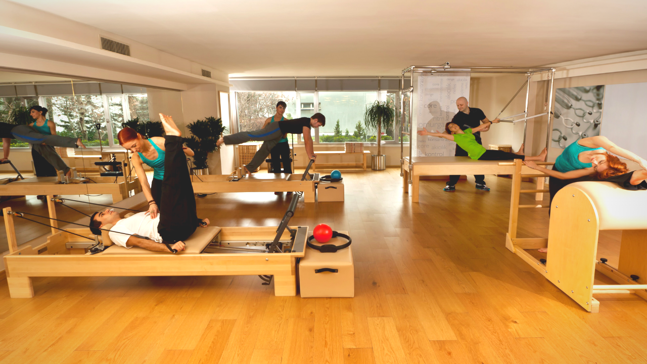 People working out in a Pilates studio with trainers.