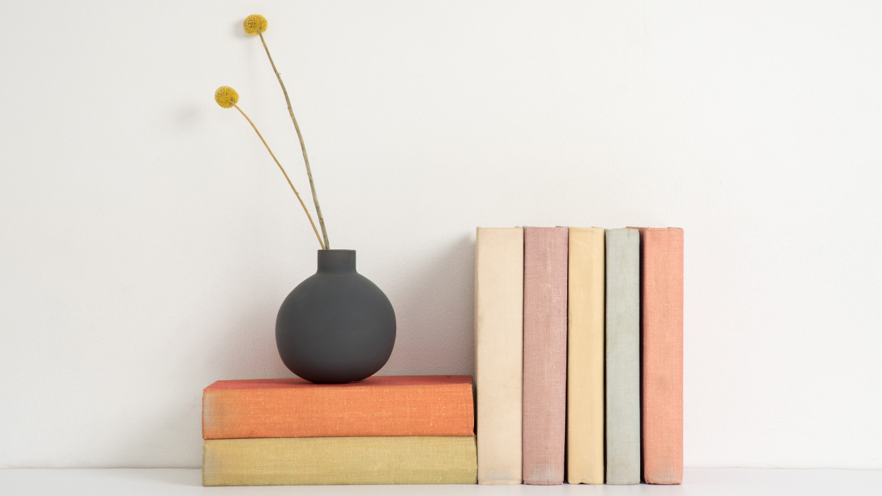 two stacked books with black vase holding 2 yellow flowers with 5 books to the right.