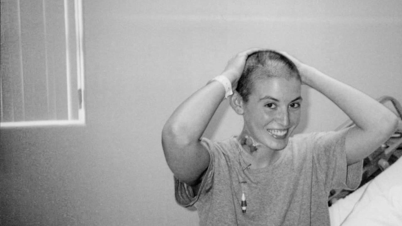 Beth in the hospital, age 20. Shaved head, hands on head, smiling with port in her neck