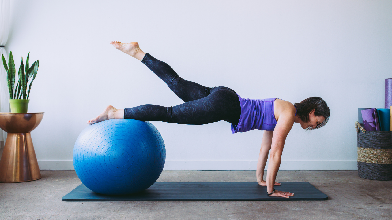 Beth wearing a purple top, black leggings in a Plank position, legs on a blue exercise ball