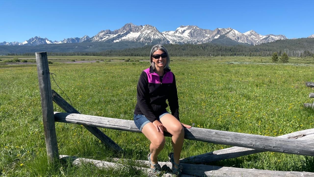 Beth sitting on fence with mountains in background
