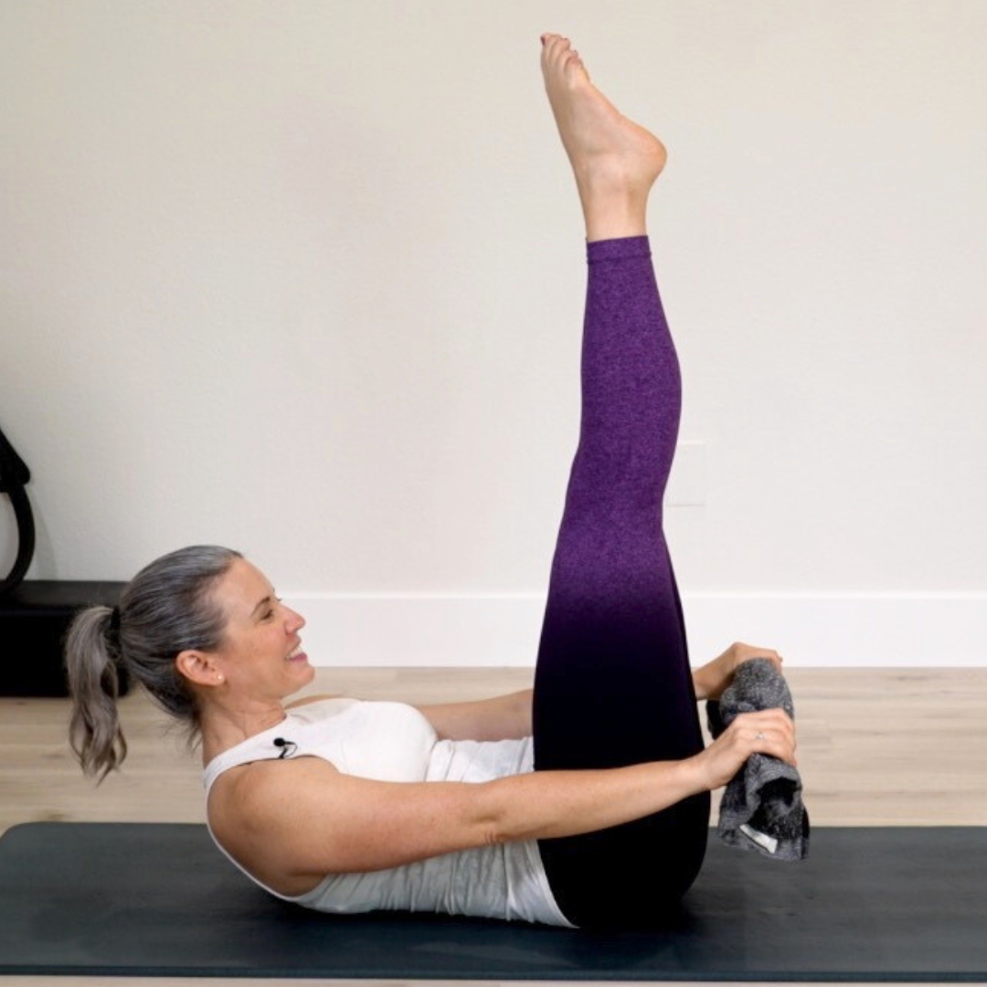 Beth on Pilates mat in hundred exercise holding towel.